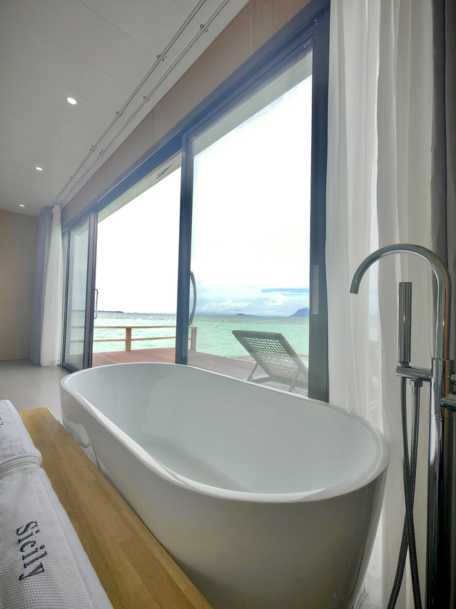 White soaking tub next to large sliding glass door at Sicily Hotel